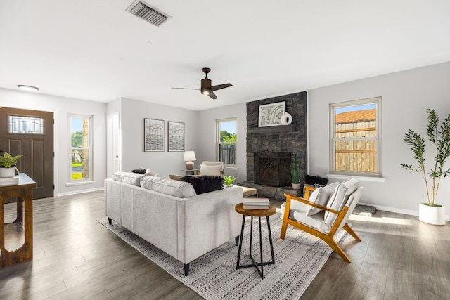 living room with wood finished floors, a stone fireplace, baseboards, and a ceiling fan