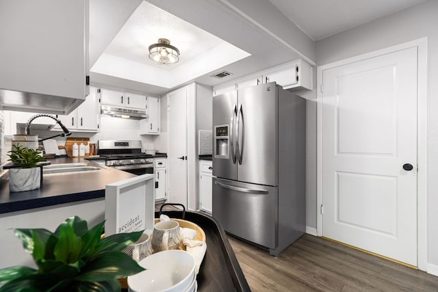 kitchen featuring stainless steel appliances, under cabinet range hood, dark wood-style floors, white cabinets, and dark countertops