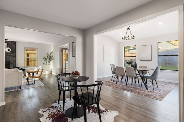 dining room with a chandelier, wood finished floors, baseboards, and a stone fireplace