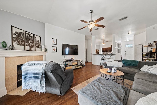 living area featuring a ceiling fan, wood finished floors, and a tile fireplace