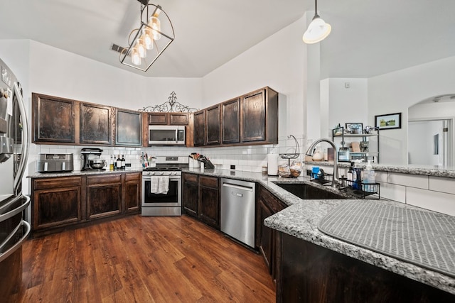 kitchen featuring stainless steel appliances, a sink, light stone counters, dark brown cabinetry, and decorative backsplash
