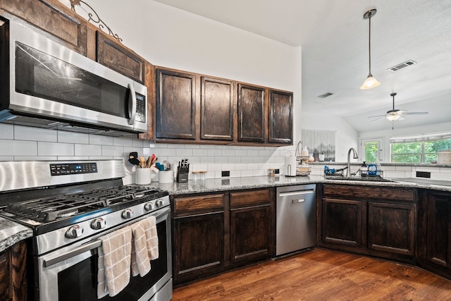 kitchen with appliances with stainless steel finishes, a sink, dark wood finished floors, backsplash, and stone countertops