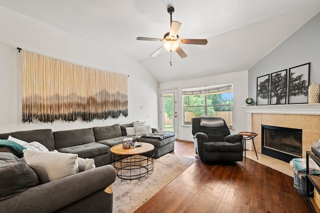 living room with vaulted ceiling, wood finished floors, a tiled fireplace, and ceiling fan