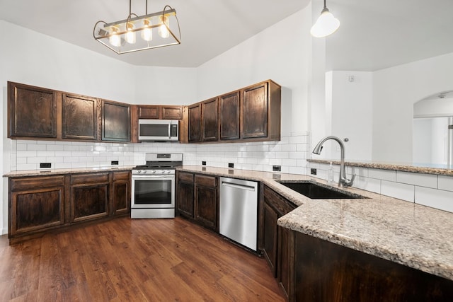 150 Primrose Blvd, Kyle, TX 78640 - kitchen featuring appliances with stainless steel finishes, light stone counters, arched walkways, tasteful backsplash, and dark brown cabinets