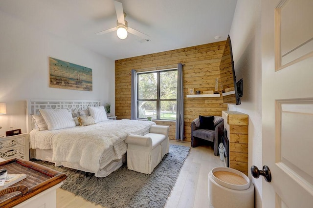 bedroom with light wood-style floors, wood walls, and ceiling fan