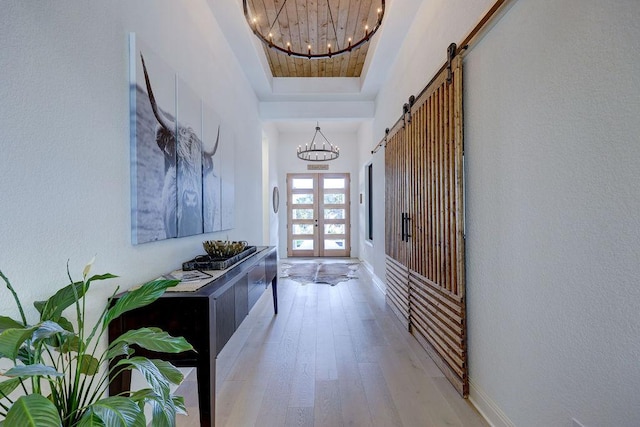hall with a chandelier, light wood-style flooring, a raised ceiling, a barn door, and baseboards