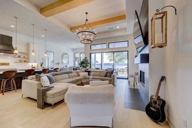 living area with light wood finished floors, beam ceiling, a chandelier, a glass covered fireplace, and recessed lighting
