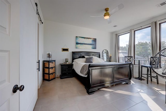 bedroom with a barn door, a ceiling fan, and light tile patterned floors