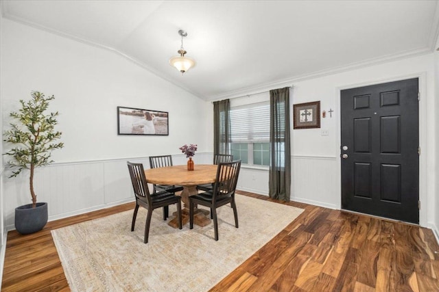 dining room with ornamental molding, vaulted ceiling, dark wood-type flooring, and wainscoting