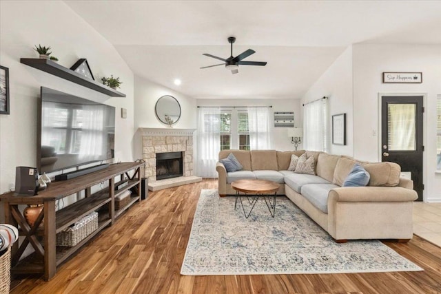 living area with a ceiling fan, vaulted ceiling, wood finished floors, and a stone fireplace