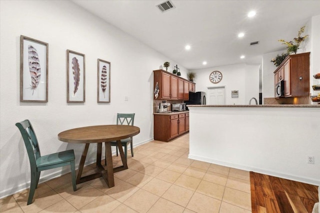 kitchen featuring stainless steel microwave, refrigerator, recessed lighting, light tile patterned floors, and brown cabinetry