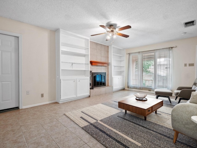 3513 Westchester Ave, Austin, TX 78759 - living room featuring a textured ceiling, a ceiling fan, built in shelves, light tile patterned floors, and a tile fireplace