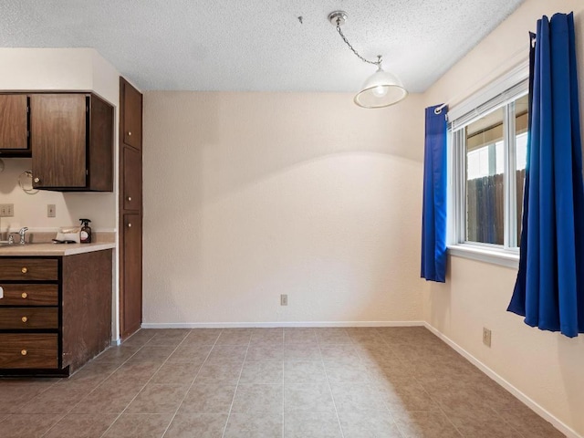 3513 Westchester Ave, Austin, TX 78759 - unfurnished dining area featuring a textured ceiling, a sink, light tile patterned flooring, and baseboards