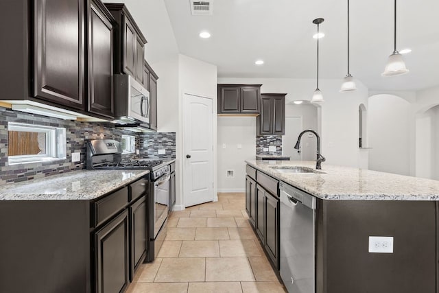 kitchen with appliances with stainless steel finishes, a sink, tasteful backsplash, a kitchen island with sink, and light stone counters