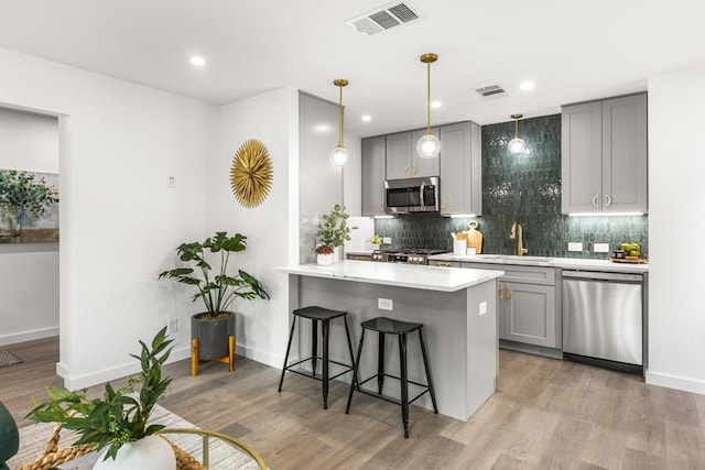 kitchen with appliances with stainless steel finishes, gray cabinets, a sink, a kitchen breakfast bar, and light countertops