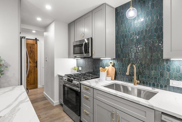 kitchen featuring appliances with stainless steel finishes, a sink, gray cabinetry, a barn door, and light stone countertops