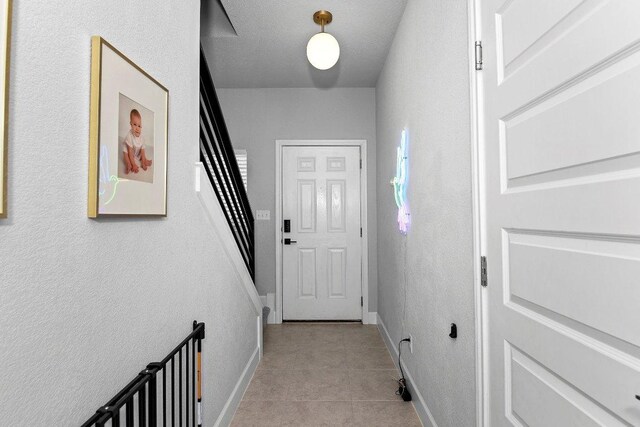 hallway featuring light tile patterned flooring, stairs, and baseboards