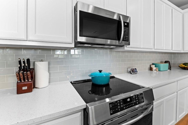 kitchen with appliances with stainless steel finishes, white cabinetry, tasteful backsplash, and light stone countertops