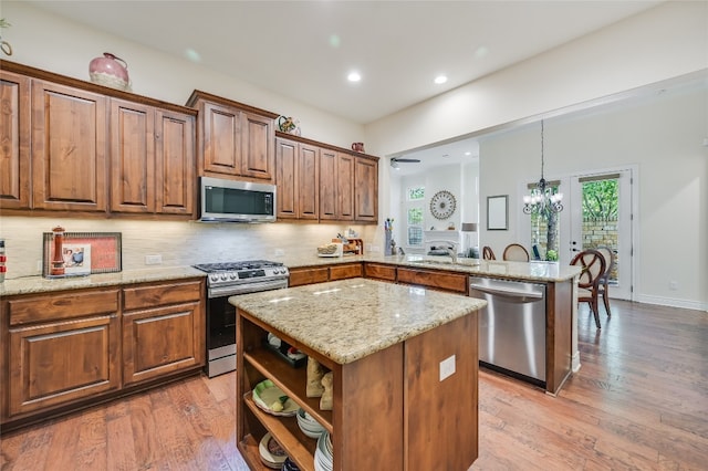 104 Rivalto Cir Unit 1, Lakeway, TX 78734 - kitchen with stainless steel appliances, a peninsula, light stone counters, tasteful backsplash, and light wood-style flooring