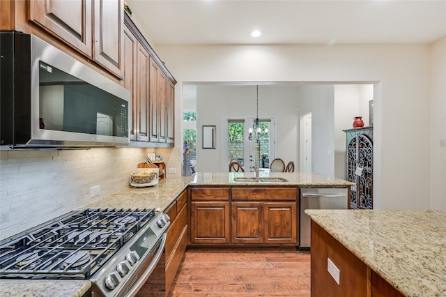 104 Rivalto Cir Unit 1, Lakeway, TX 78734 - kitchen featuring stainless steel appliances, light wood-style floors, a chandelier, light stone counters, and decorative backsplash