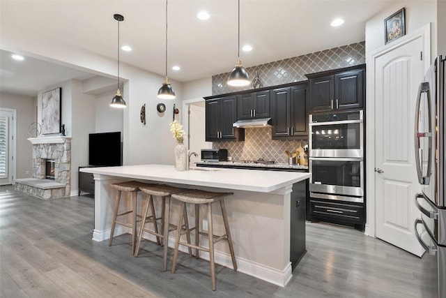 225 Escarpment Way, Cedar Park, TX 78613 - kitchen with appliances with stainless steel finishes, under cabinet range hood, a breakfast bar, tasteful backsplash, and light countertops