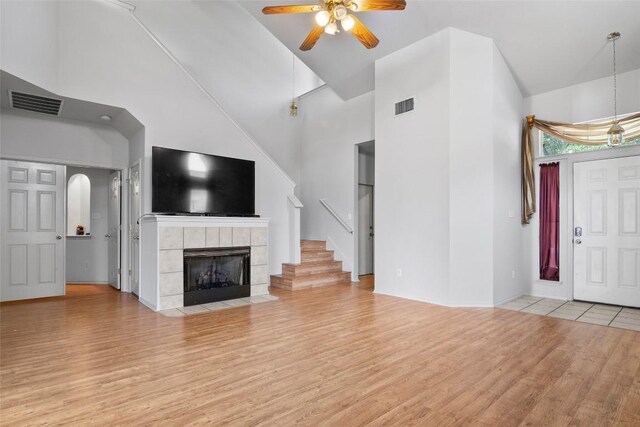 3908 Whitey Ford Way, Round Rock, TX 78665 - unfurnished living room with light wood-type flooring, ceiling fan, high vaulted ceiling, a tiled fireplace, and stairs