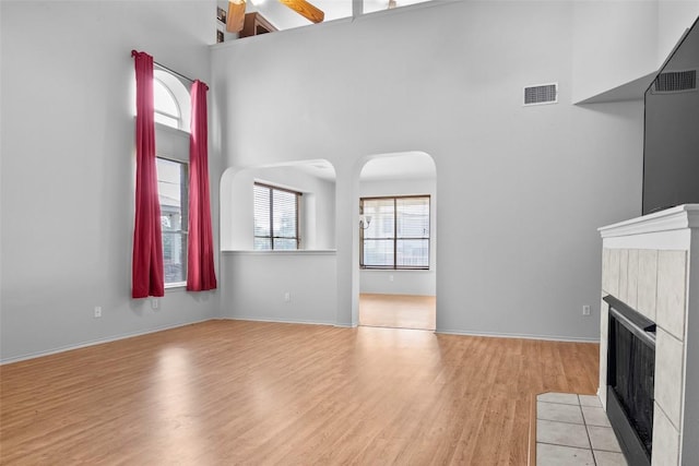 3908 Whitey Ford Way, Round Rock, TX 78665 - unfurnished living room featuring a towering ceiling, light wood finished floors, a fireplace, and arched walkways