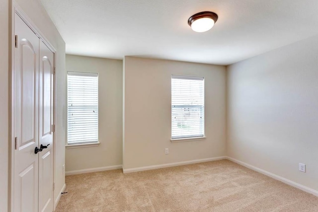 empty room featuring healthy amount of natural light, light colored carpet, and baseboards