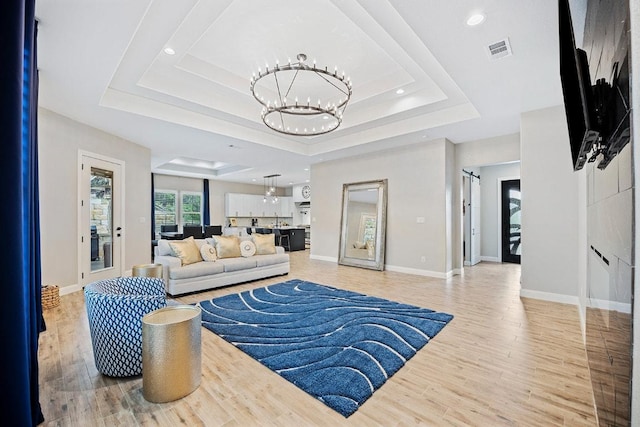 living area featuring a chandelier, a raised ceiling, light wood-style flooring, baseboards, and recessed lighting