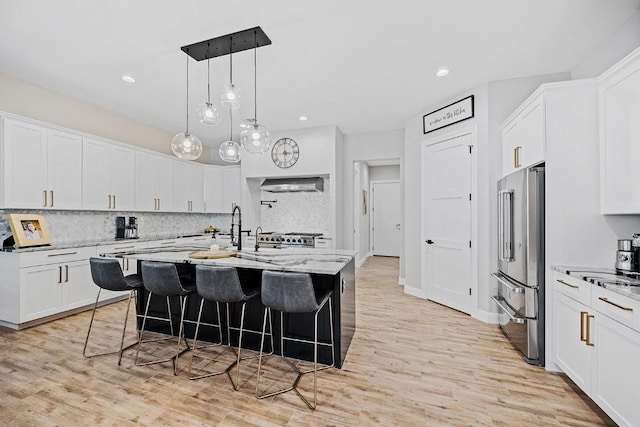kitchen featuring high end refrigerator, ventilation hood, a breakfast bar area, white cabinetry, and recessed lighting