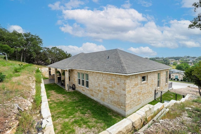 rear view of house featuring stone siding and roof with shingles
