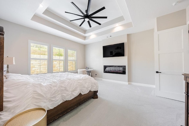bedroom featuring a raised ceiling, carpet, a glass covered fireplace, and a ceiling fan