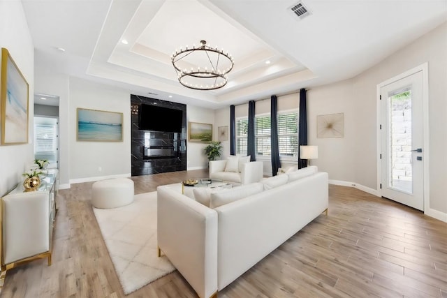living room with wood finished floors, a chandelier, healthy amount of natural light, and a raised ceiling