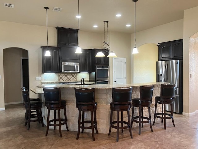 129 S Abrego Xing, Floresville, TX 78114 - kitchen with stainless steel appliances, arched walkways, backsplash, dark cabinets, and a large island with sink