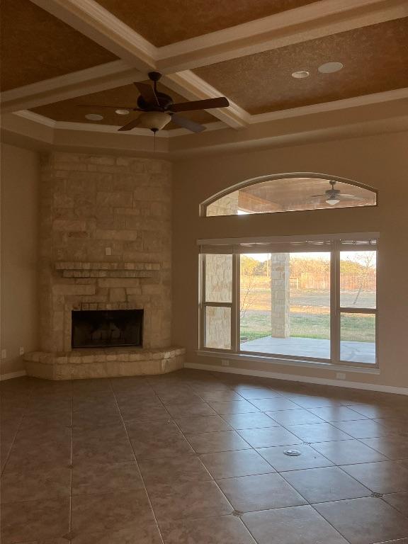 129 S Abrego Xing, Floresville, TX 78114 - unfurnished living room featuring ceiling fan, coffered ceiling, tile patterned flooring, beam ceiling, and a stone fireplace