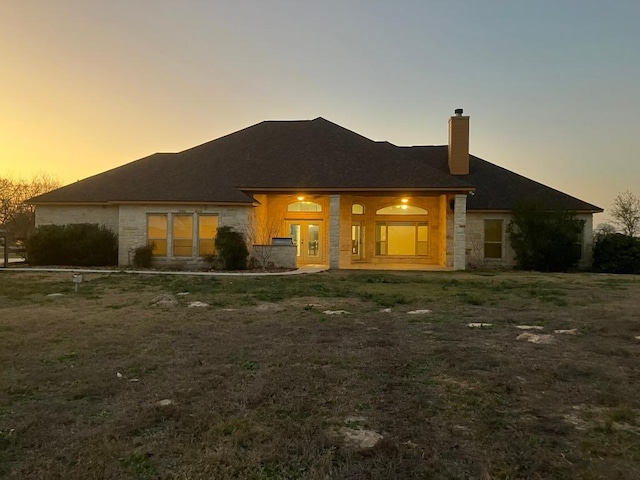 129 S Abrego Xing, Floresville, TX 78114 - back of house at dusk featuring stone siding and a chimney