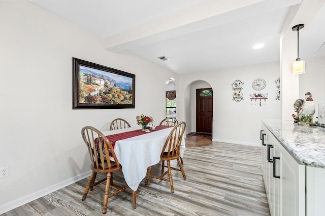 dining space featuring arched walkways, light wood-style floors, baseboards, and beamed ceiling