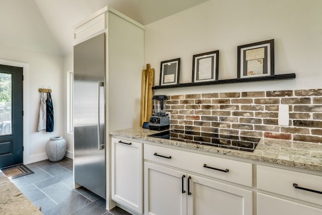 1305 Quail Ravine, Round Rock, TX 78664 - kitchen featuring backsplash, vaulted ceiling, white cabinetry, light stone counters, and black electric stovetop