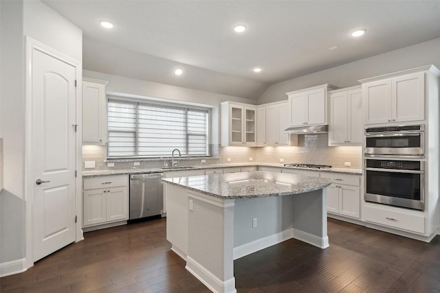 kitchen with stainless steel appliances, a sink, under cabinet range hood, white cabinets, and vaulted ceiling