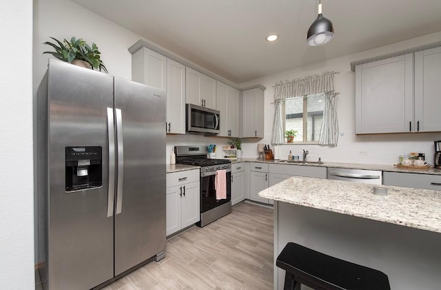 500 Pickrell Loop, Liberty Hill, TX 78642 - kitchen featuring appliances with stainless steel finishes, light stone countertops, a sink, a breakfast bar, and light wood-style floors
