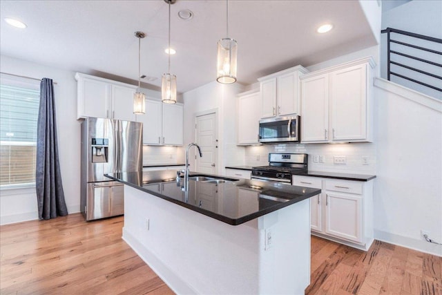 kitchen with appliances with stainless steel finishes, a sink, dark countertops, a center island with sink, and light wood-style floors