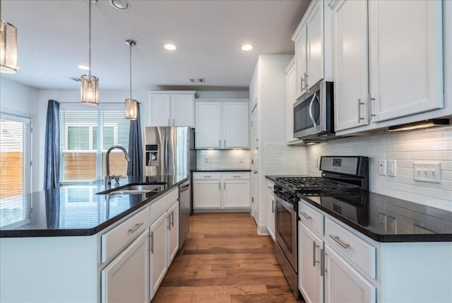 kitchen featuring appliances with stainless steel finishes, a sink, wood finished floors, white cabinetry, and recessed lighting