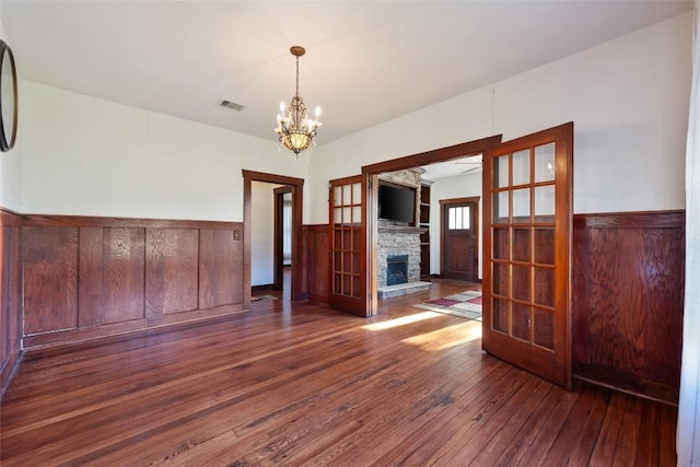117 N Main St, Paige, TX 78659 - empty room with hardwood / wood-style flooring, a chandelier, a wainscoted wall, and a stone fireplace