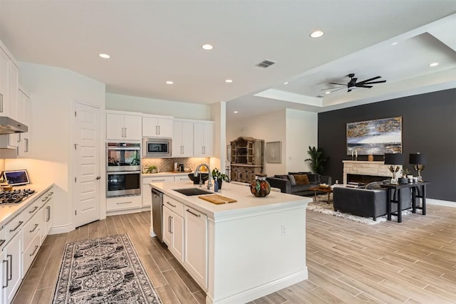 kitchen with a sink, stainless steel appliances, wood finish floors, light countertops, and white cabinetry
