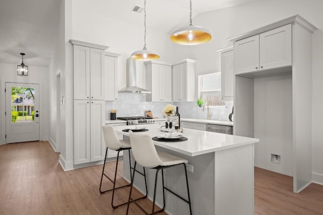 kitchen with wall chimney exhaust hood, decorative backsplash, a breakfast bar, light wood-style flooring, and hanging light fixtures