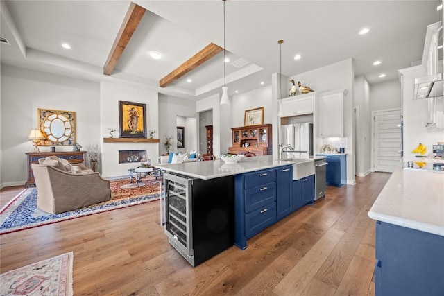 kitchen with blue cabinets, open floor plan, a sink, white cabinetry, and light wood-style floors