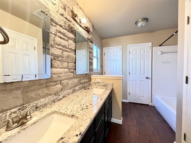 bathroom featuring wood finished floors, double vanity, shower / bath combination, baseboards, and backsplash