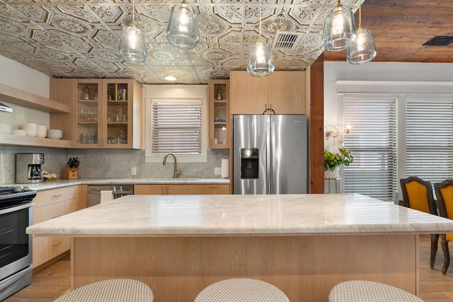 1307 E 2nd St, Austin, TX 78702 - kitchen featuring stainless steel appliances, a sink, light wood-style flooring, backsplash, and a breakfast bar