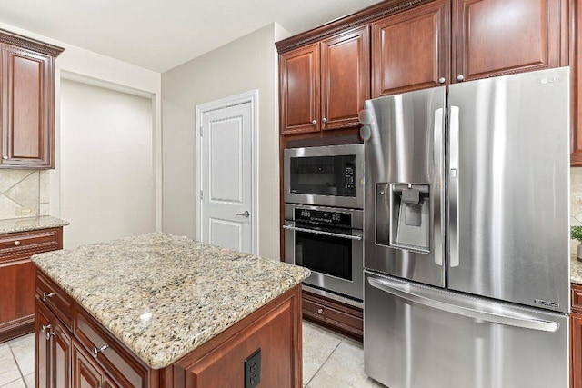 307 Palmetto Dr, Georgetown, TX 78633 - kitchen featuring appliances with stainless steel finishes, light stone counters, a center island, light tile patterned flooring, and decorative backsplash