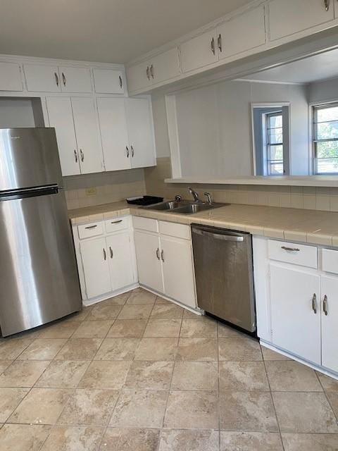 kitchen with appliances with stainless steel finishes, a sink, tile counters, and white cabinetry